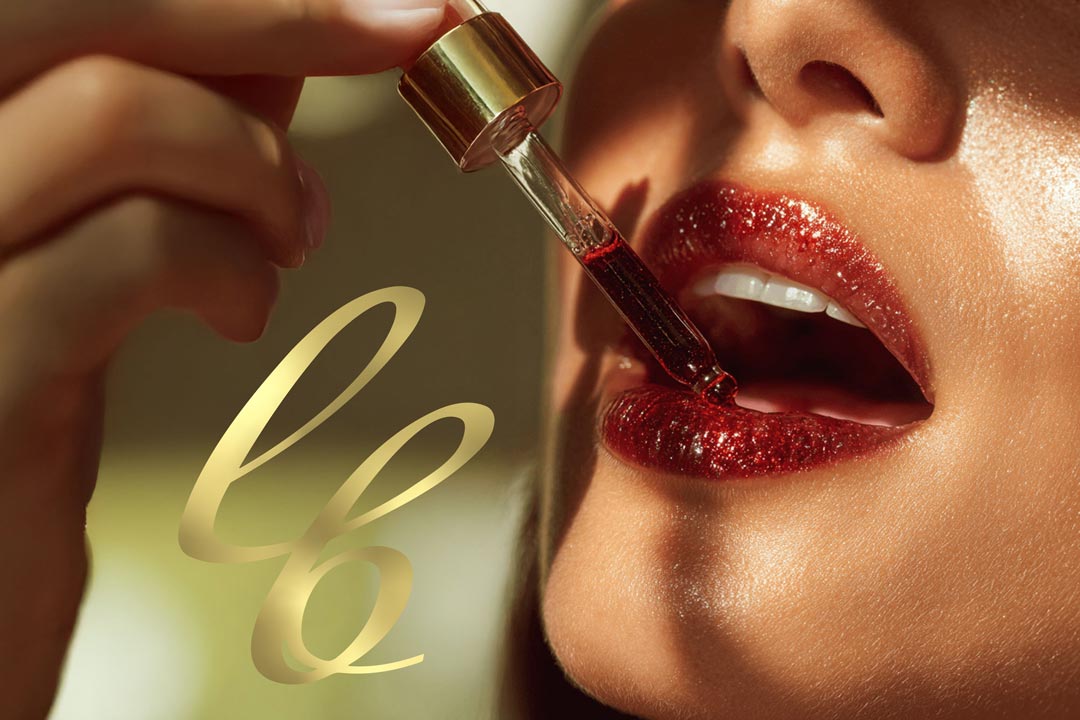 Close-up of a person applying red lip gloss to their lips with Luxe Beauty logo in the background. Website built by G&V Venture Brands Bristol.